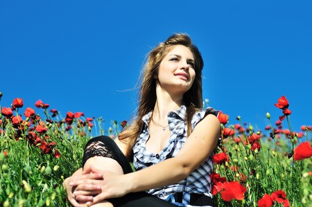 beautiful girl with long hair sitting in the poppy field の写真素材