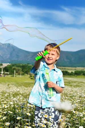 funny little boy blowing soap bubbles  in daisy fieldの写真素材