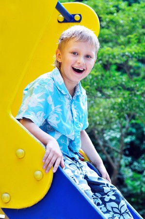 funny boy on a blue-yellow playground slide の写真素材