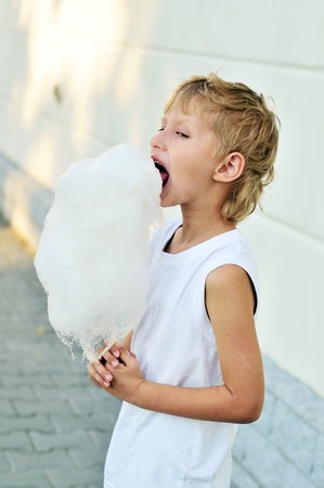 funny boy eating and enjoying cotton candy outdoorsの写真素材