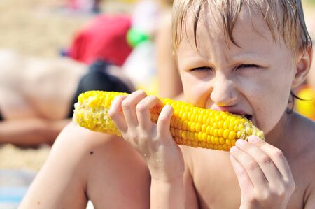boy eating fresh boiled corn on the beachの写真素材