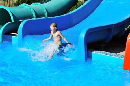 Cute little boy sliding down a water slide to poolの写真素材