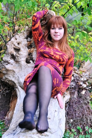 redheaded girl sitting on the log in forest の写真素材