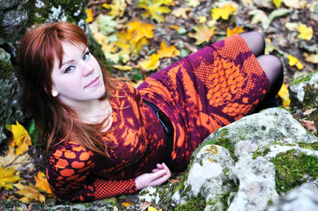 redheaded girl sitting near stones and  autumn leavesの写真素材