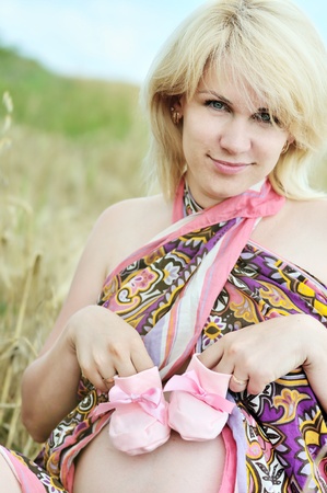 pregnant woman laying in wheat field with pink bootee on tummyの写真素材