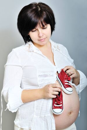 pensive pregnant woman with baby's shoes on her bellyの写真素材