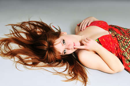young woman with red hair splayed around her head over the gray backgroundの写真素材