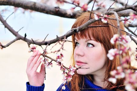 redheaded girl smelling blossom of peach tree の写真素材