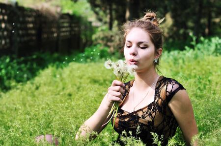 teen elegant pretty girl blowing on many dandelions の写真素材