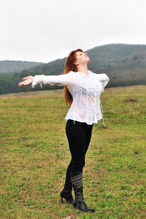 redheaded girl standing in field at one with nature, boughs reach out towards the rainの写真素材