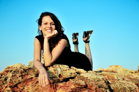 happy brunette girl laying on the cliff at sunset time の写真素材