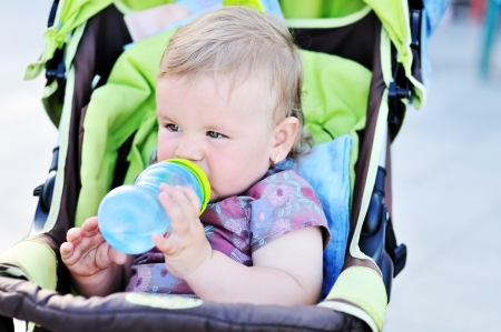 baby girl sitting in the stroller and drinking wateの写真素材