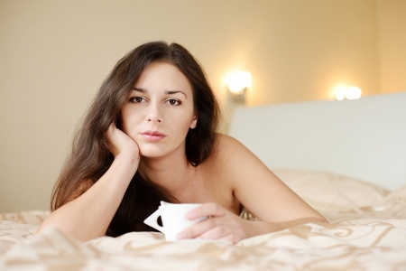brunette lady enjoying coffee in the bedの写真素材