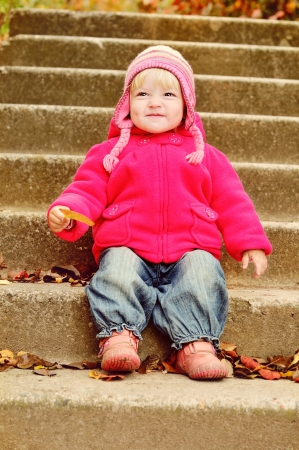 toddler girl with leaf sitting on the stairsの写真素材