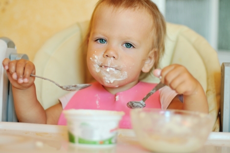 baby girl eating with two spoonsの写真素材