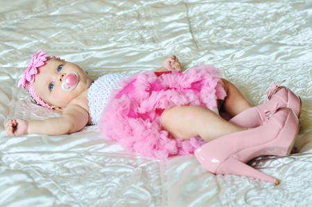 fashion 3 months old baby girl laying on the bed with high heels shoesの写真素材