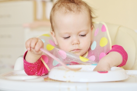 baby girl eating with spoon and handの写真素材