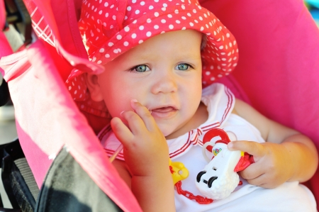funny baby girl sitting in red strollerの写真素材