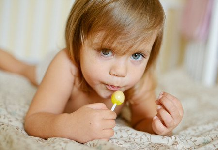 toddler with lollypop lying on the bedの写真素材
