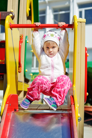 toddler girl on the playground hanging on the barの写真素材