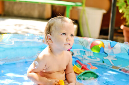 baby girl sitting in the pool on the yard of homeの写真素材