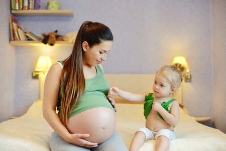 mother and her baby daughter waiting for newborn and showing tummies (focus on baby girl)の写真素材