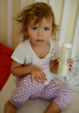 toddler girl with bottle of milk in bedの写真素材