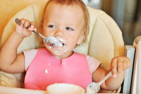 baby girl eating with two spoonsの写真素材