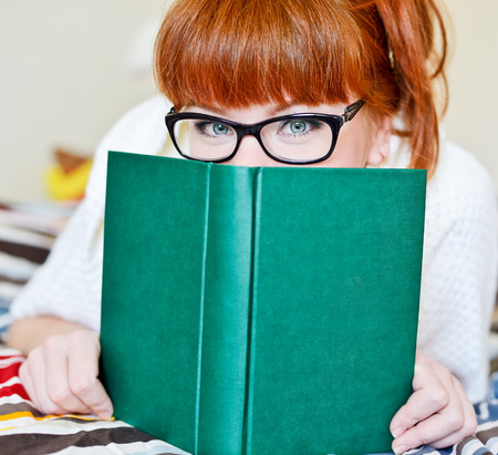 happy student hiding face behind the bookの写真素材