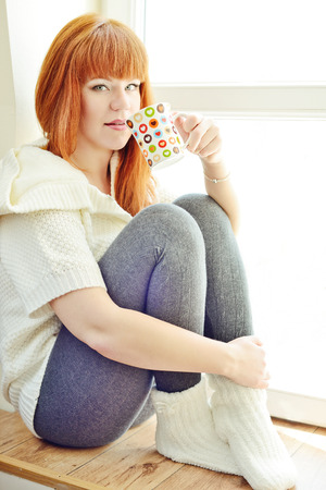 redhead young woman resting near the window with cup of teaの写真素材