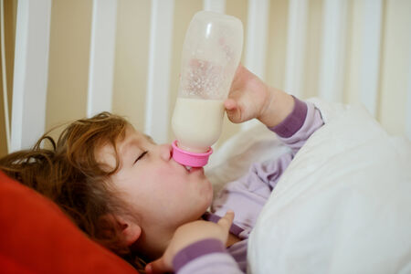 toddler with bottle lying in bedの写真素材
