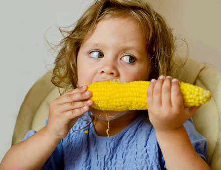funny toddler girl eating cornの写真素材
