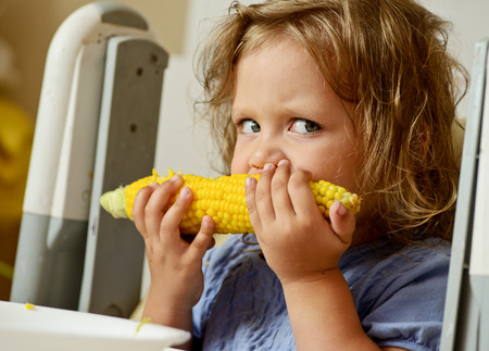 funny toddler girl eating cornの写真素材