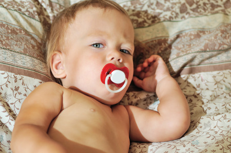 toddler with pacifier lying on bedの写真素材