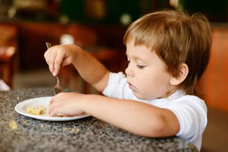 toddler girl is eating with fork in cafeの写真素材