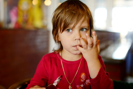 little girl in cafe licking her fingers after mealの写真素材
