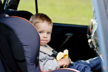 toddler boy sitting in the car seat and eating a bananaの写真素材
