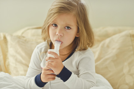 little girl with cough using inhaler at homeの写真素材