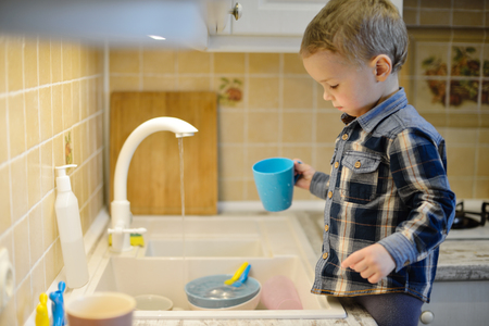 little boy helping mother washing dishes in the kitchenの写真素材