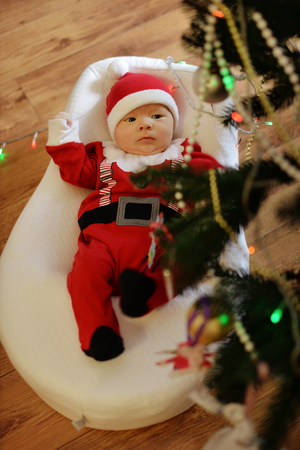 Portrait of newborn baby boy wearing Santa clothes under tthe Christmas treeの写真素材