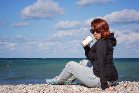 redhead woman with coffee relaxing near the seaの写真素材