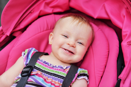 happy baby girl sitting in pink strollerの写真素材