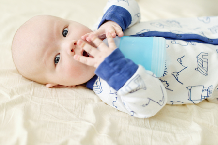 baby  drinking water from bottle lying on bedの写真素材