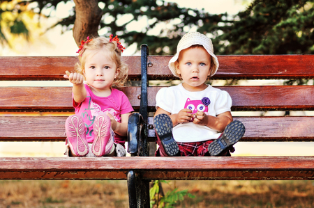two baby friends sitting on the benchの写真素材