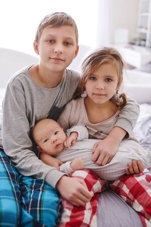 big brother and sister playing with baby brother at homeの写真素材