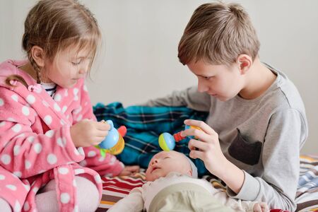 big brother and sister playing with baby brother at homeの写真素材