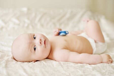 happy baby with pacifier in hand on the bedの写真素材