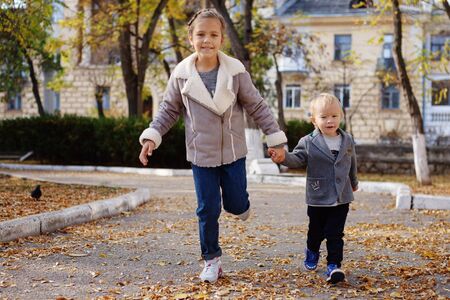 sister and toddler brother running in the fall park, focus on the brothers faceの写真素材