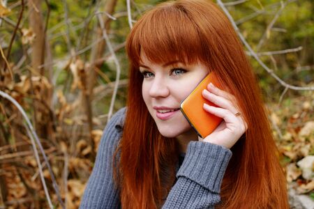 redhead young woman with mobile phone outdoorsの写真素材
