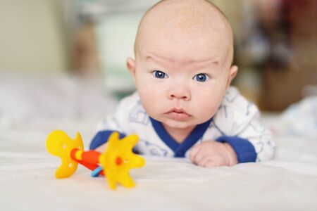 funny baby with rattle on the bedの写真素材